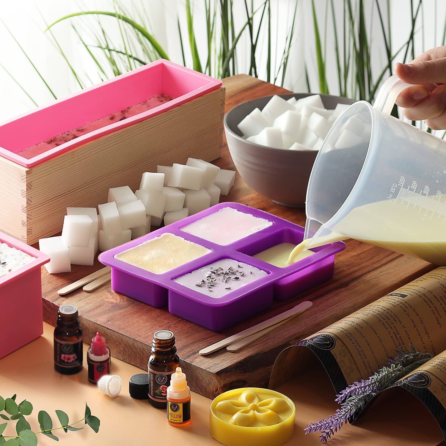 Soap making kit ingredients and tools laid out on a wooden board, with liquid being poured into a silicone mold.