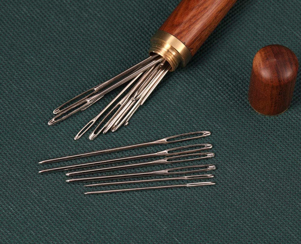 Set of large eye blunt darning needles spilling from a wooden storage case with a cap nearby.