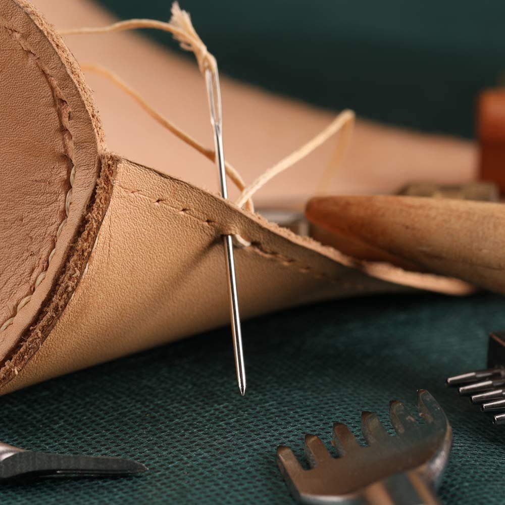 Close-up of a large eye blunt needle stitching leather with thread, showing leathercraft tools.
