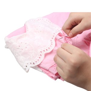 Hands sewing a pink garment with white lace trim using a needle and thread.