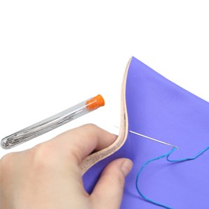 Hand holding a storage bottle of sewing needles and stitching purple leather with a needle and blue thread