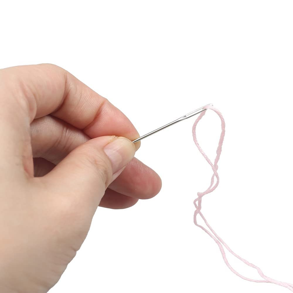 Hand threading pink yarn through the eye of a sewing needle against a white background.