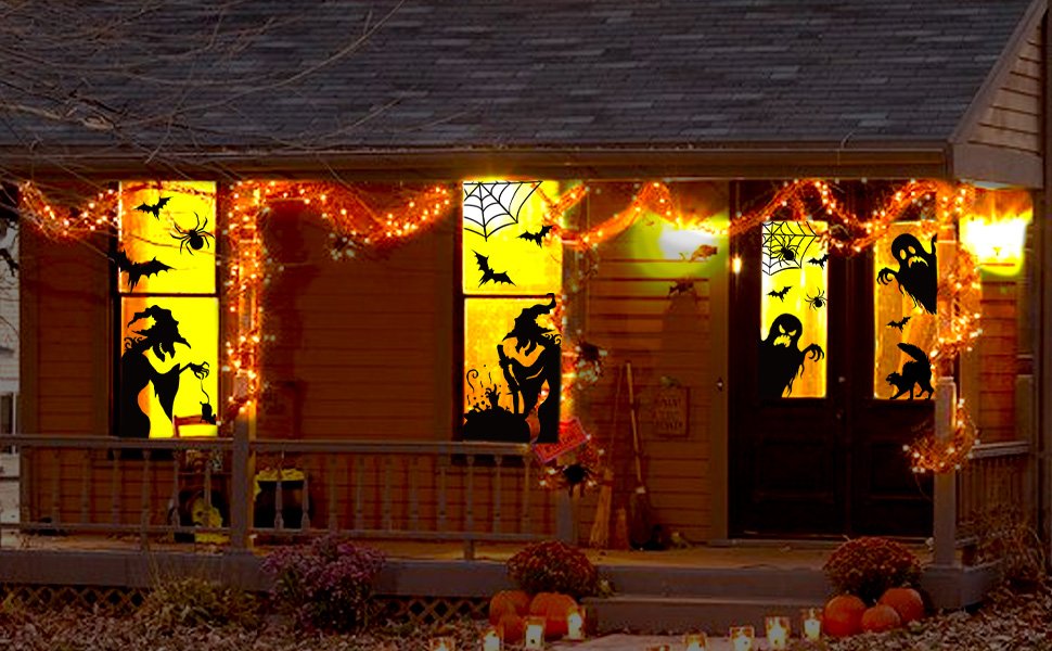 Halloween window clings featuring witches, bats, spiders, ghosts, and webs applied to a house exterior with orange string lights.