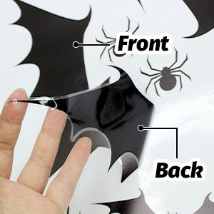 Hand peeling a large Halloween window cling featuring bats and spiders, showing front and back sides.