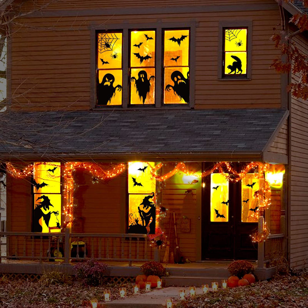 Halloween window clings of ghosts, bats, spiders, witches, and cats decorating a house at night.