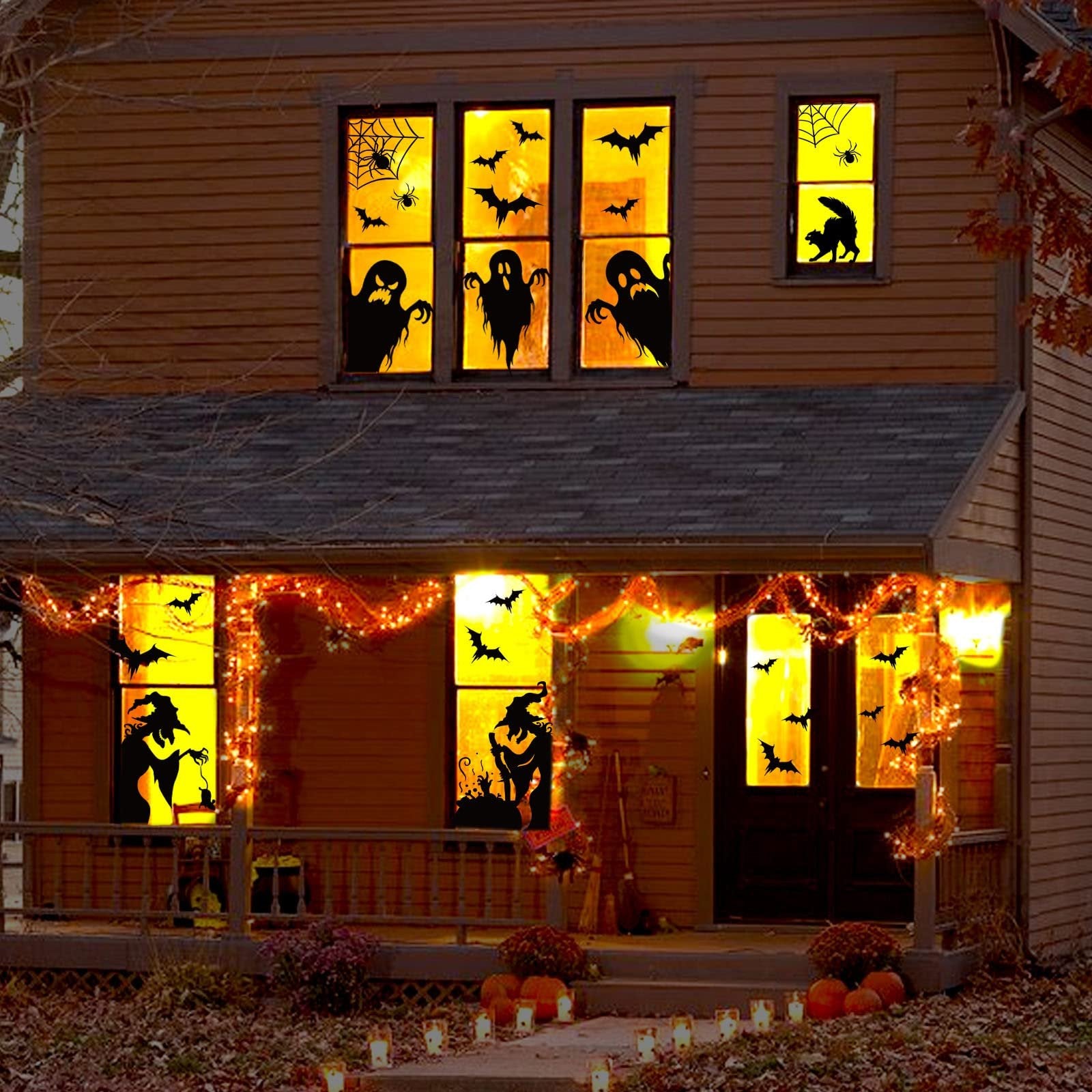 Halloween window clings of ghosts, bats, spiders, witches, and cats decorating a house at night.