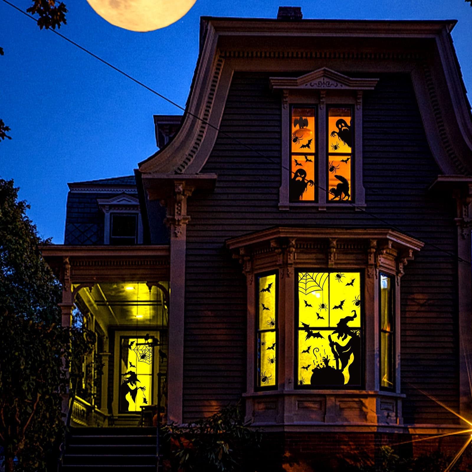 Victorian house at night decorated with Halloween window clings of ghosts, bats, spiders, and witches.