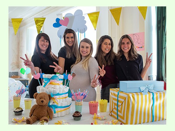 Five women celebrating a baby shower with a diaper cake, gifts, and decorations.