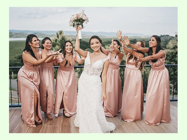Bride holding bouquet with bridesmaids in pink dresses celebrating on a balcony