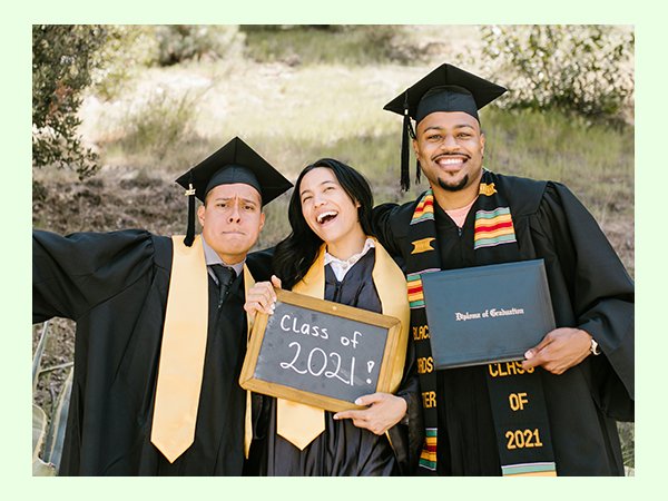 Three smiling graduates in caps and gowns pose outdoors, one holding a diploma and another a chalkboard sign that reads 'Class of 2021!'