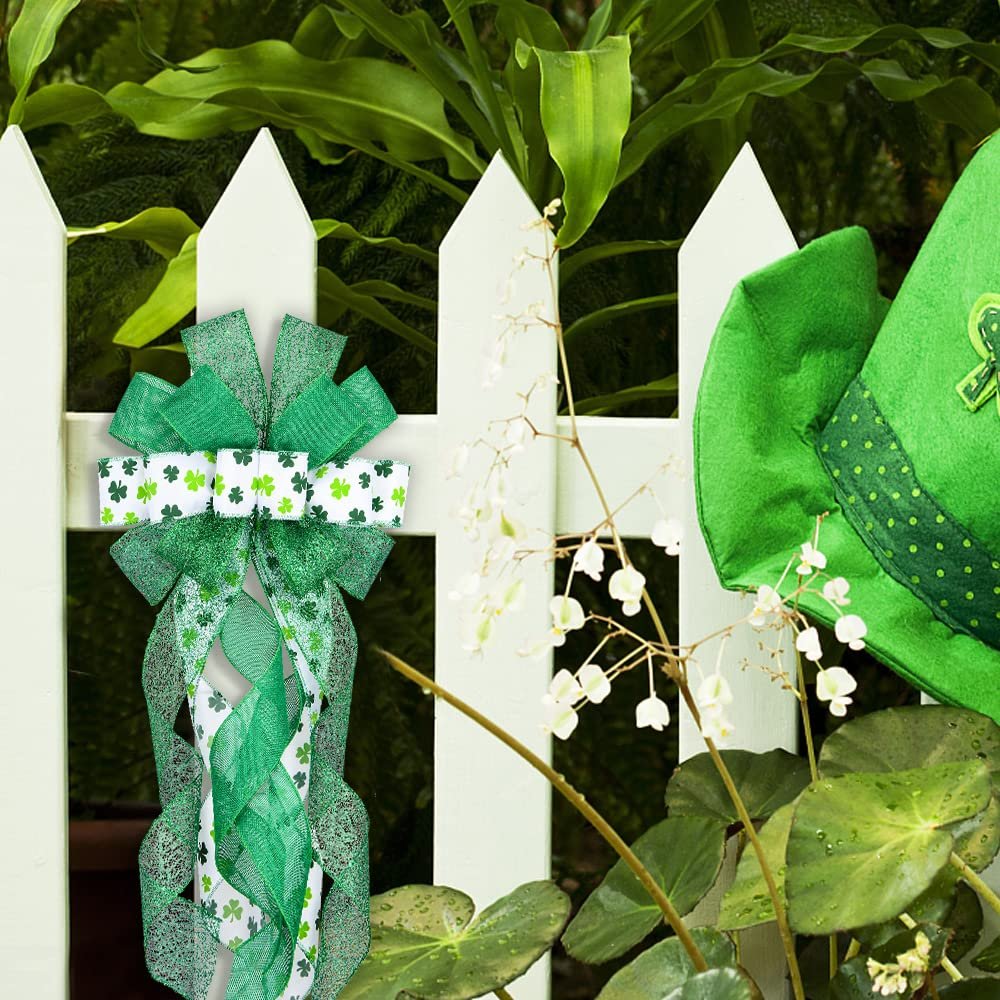 Green glitter plaid St. Patrick's Day bow with shamrock pattern ribbons hanging on a white picket fence next to a green hat.