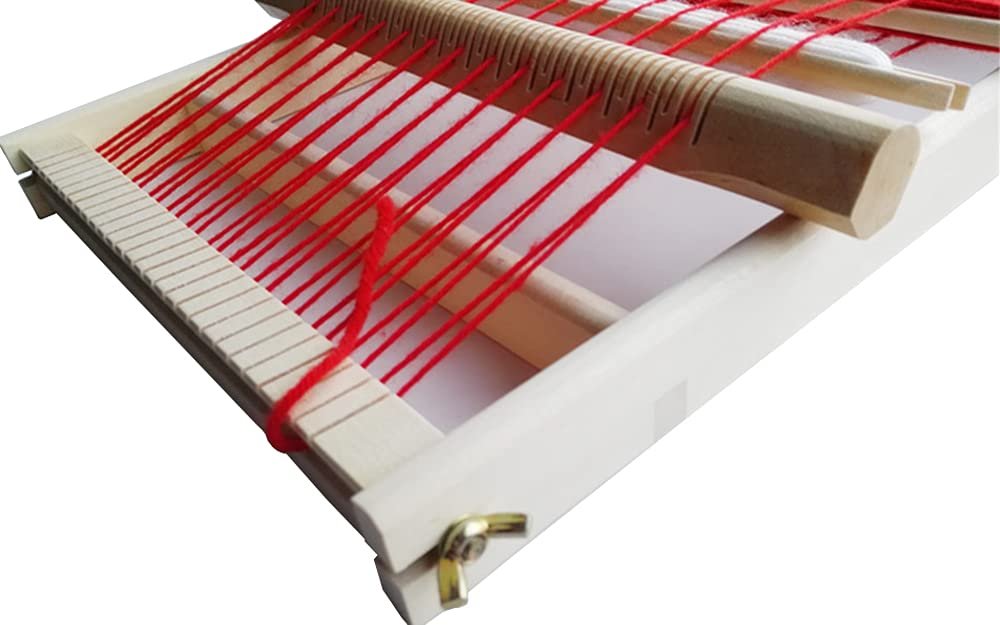 Close-up of a wooden weaving loom with red yarn threaded through the heddles and warp threads.