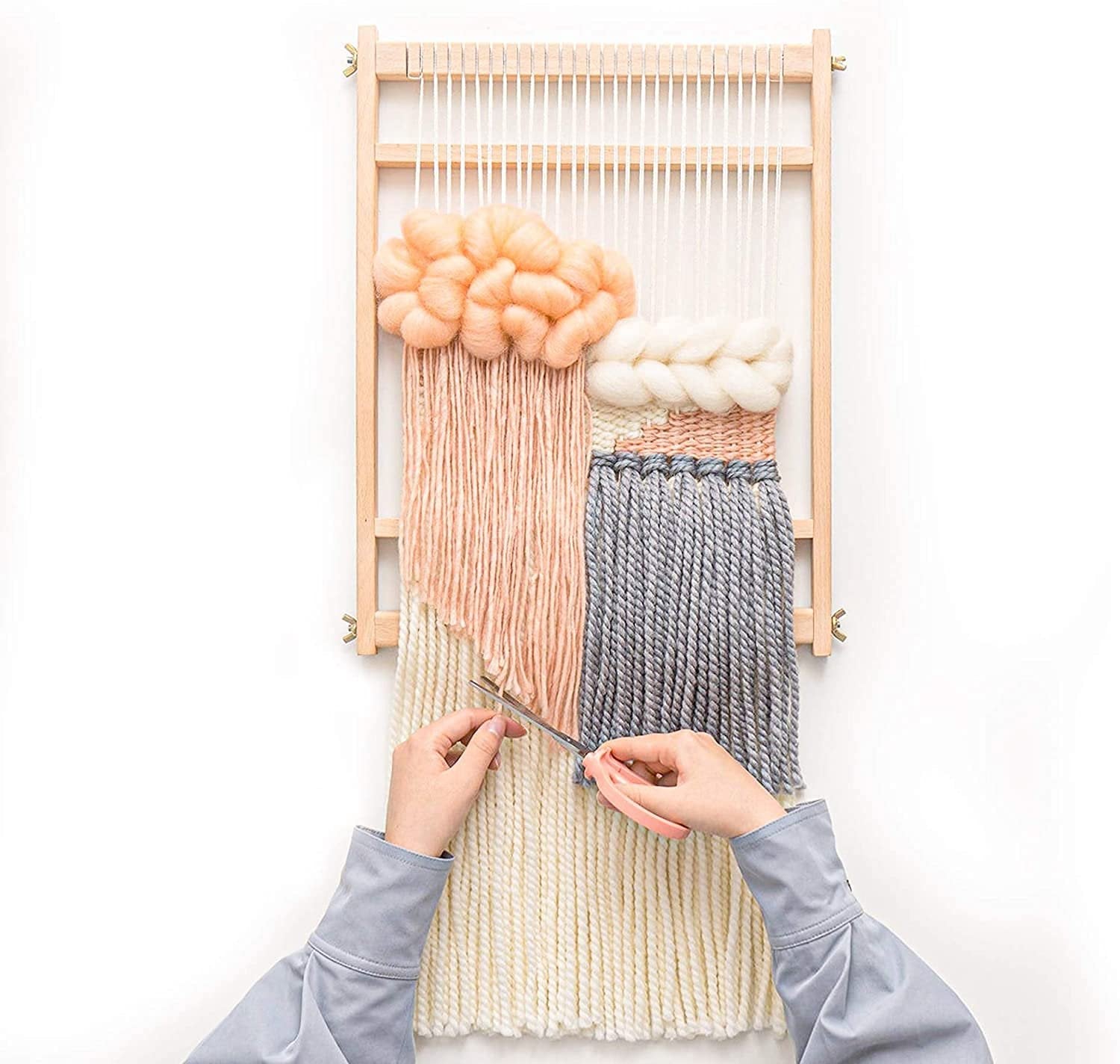 Hands using scissors to cut yarn on a wooden weaving loom with a partially completed tapestry
