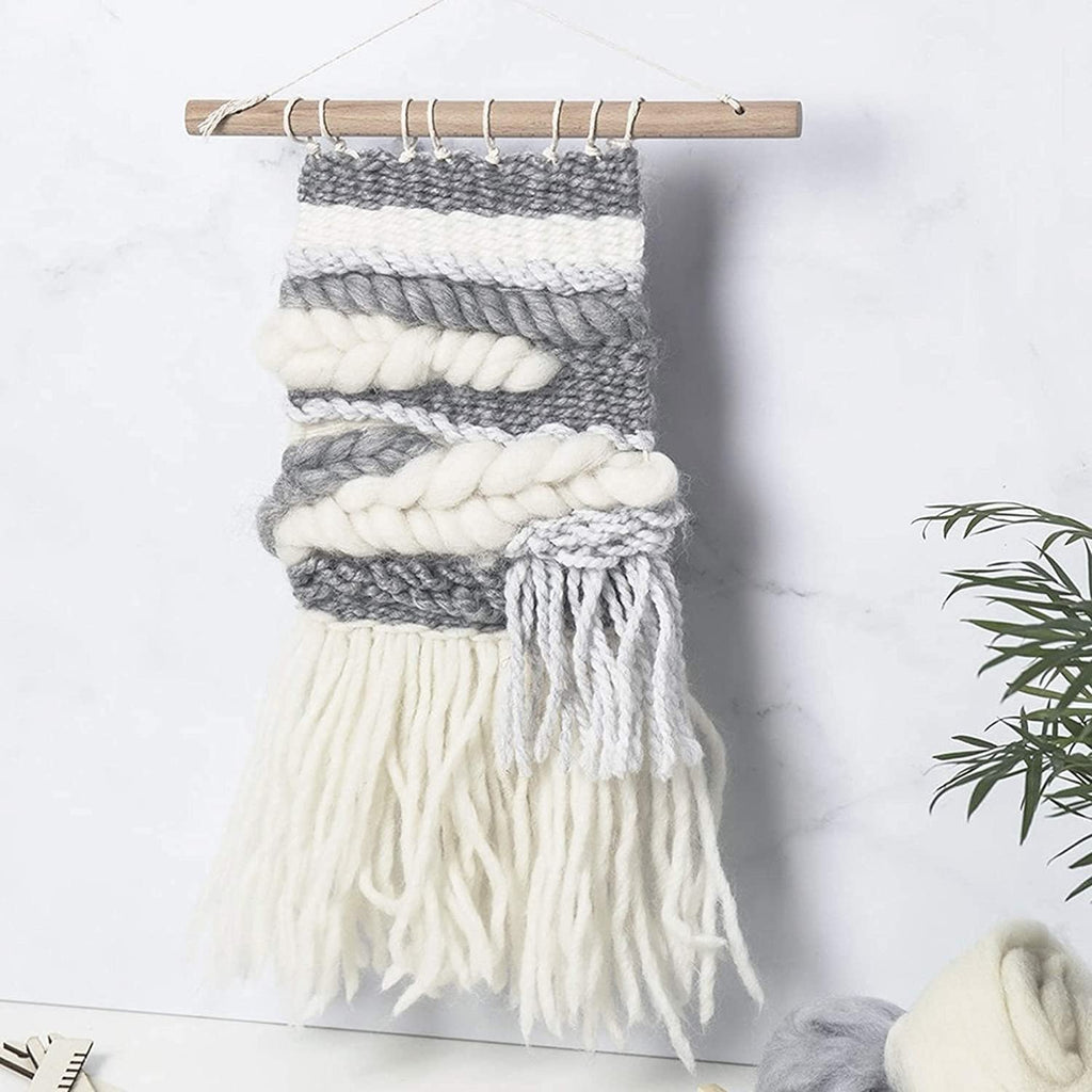Woven wall hanging with grey and white yarn on a wooden dowel against a marble background.