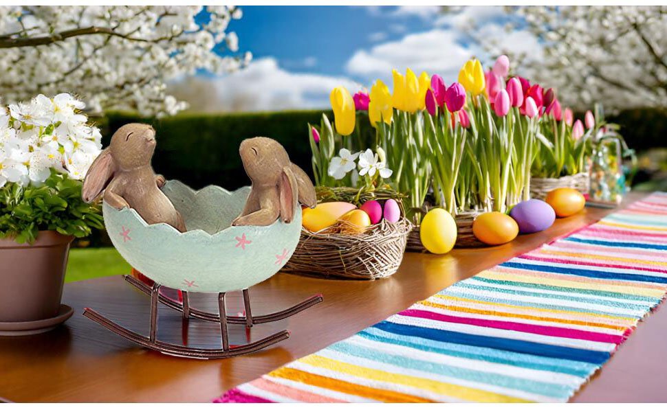 Easter table setting with two bunny figurines in an egg cradle, colorful tulips, and decorative eggs.