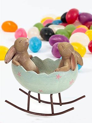 Easter egg cradle figurine with two bunnies inside, surrounded by colorful jelly beans.