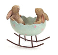 Two laughing bunny rabbits in a light blue Easter egg cradle on a rocking base, decorated with pink starbursts.