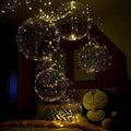 Clear LED light-up balloons with warm white string lights floating indoors, near a bed with pillows and a stuffed toy.