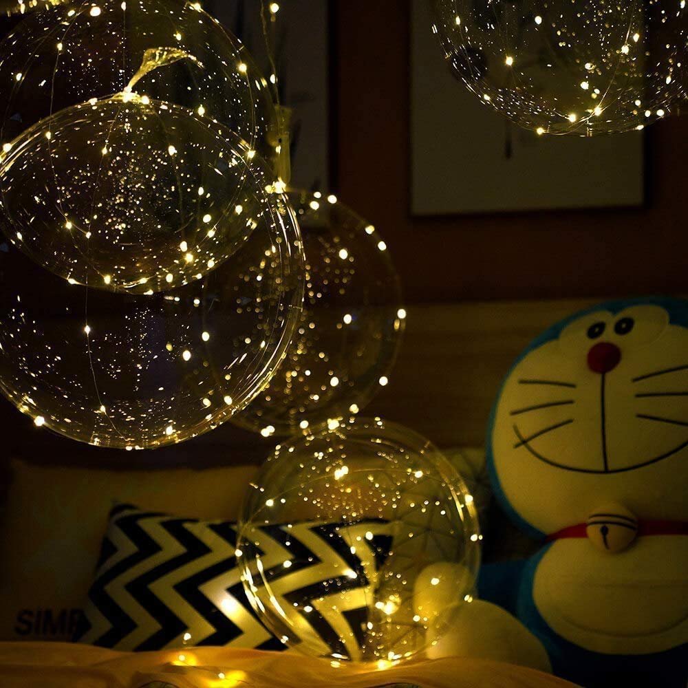 Clear LED light-up balloons with warm white string lights, arranged indoors with a stuffed toy.