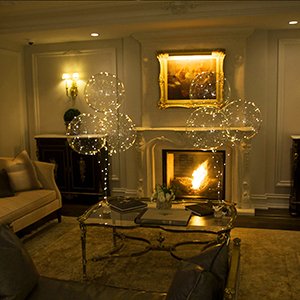 Four clear LED light-up bobo balloons floating in a living room with a fireplace