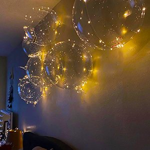 Several clear LED light-up bobo balloons with warm white string lights attached, floating on a wall.
