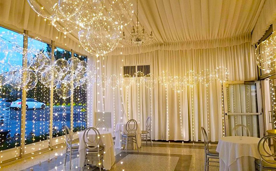 Clear LED light-up bobo balloons hanging in a decorated room with tables and chairs