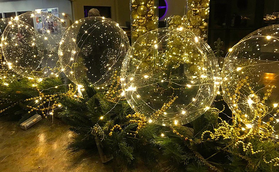 Clear LED light-up bobo balloons nestled in evergreen branches with gold beaded garland