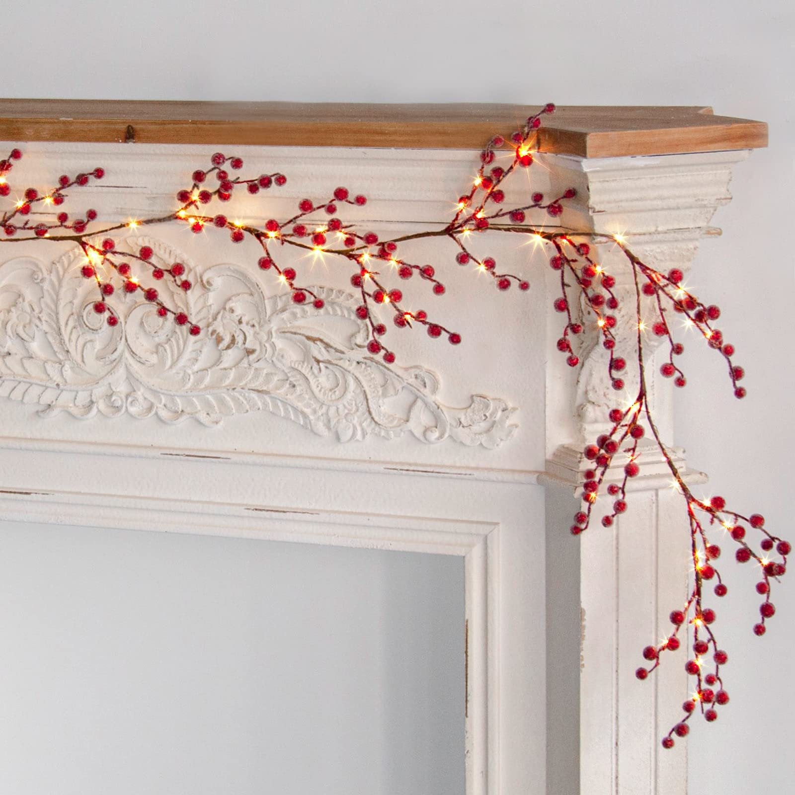 Lighted red berry garland with warm white LED lights draped over a decorative white mantelpiece.