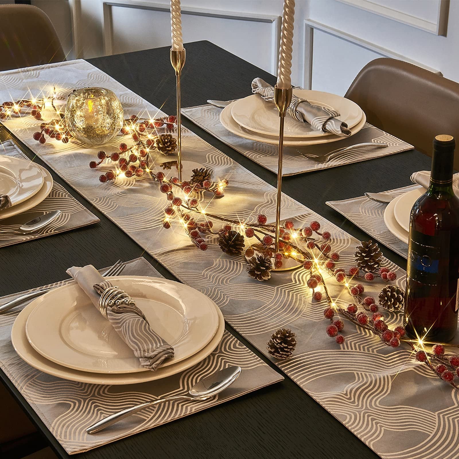 Lighted berry and pinecone garland draped across a table runner with place settings.