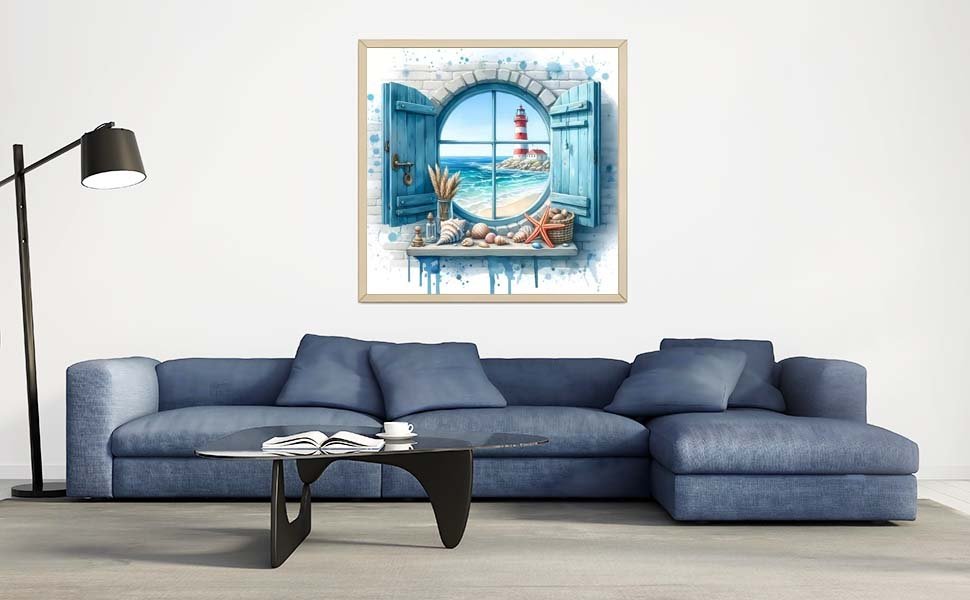 Framed lighthouse beach scene artwork hanging above a blue sectional sofa, featuring a round window view of a lighthouse and ocean.