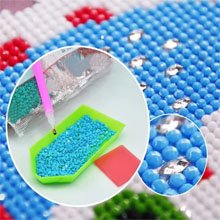 Diamond painting kit showing blue and white beads, a pink applicator tool, and a green tray with blue beads.