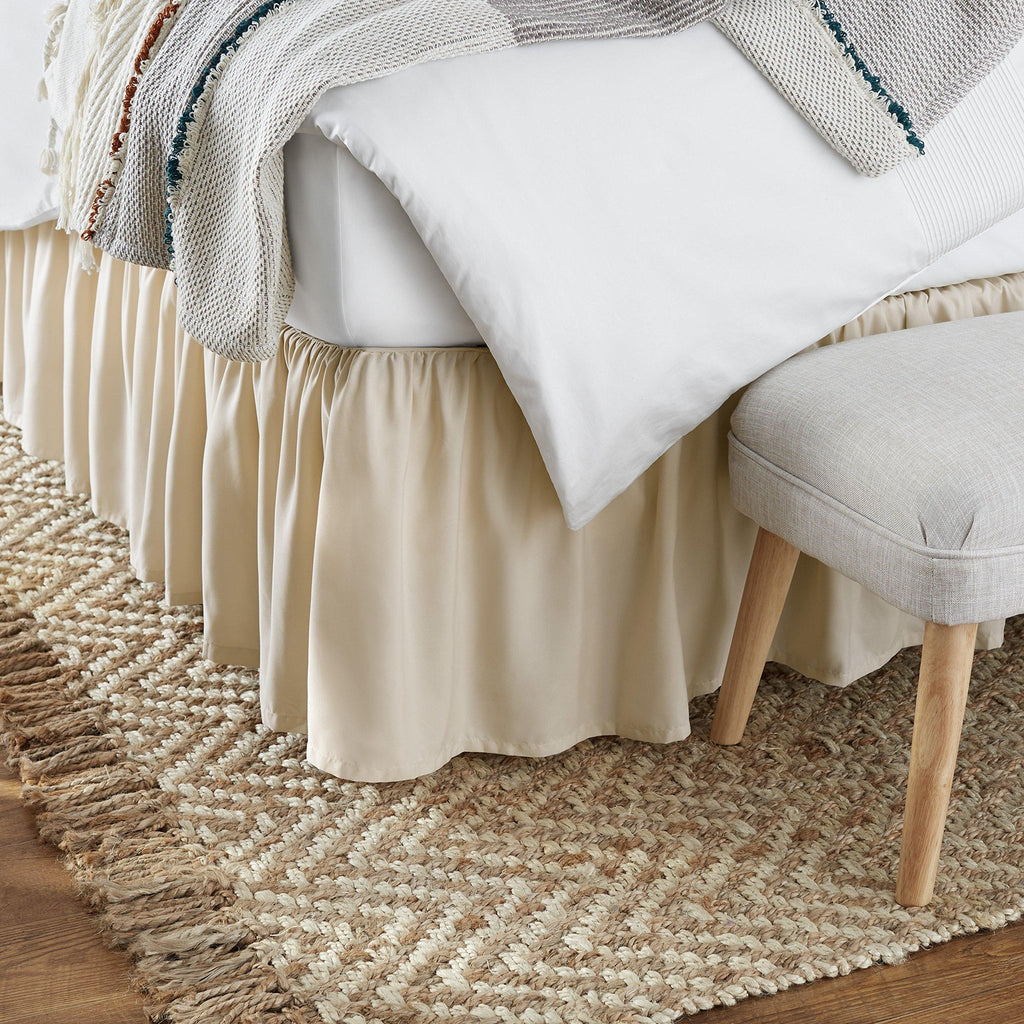 Bed skirt with ruffles and a woven throw blanket draped over the bed, shown with a stool and rug.