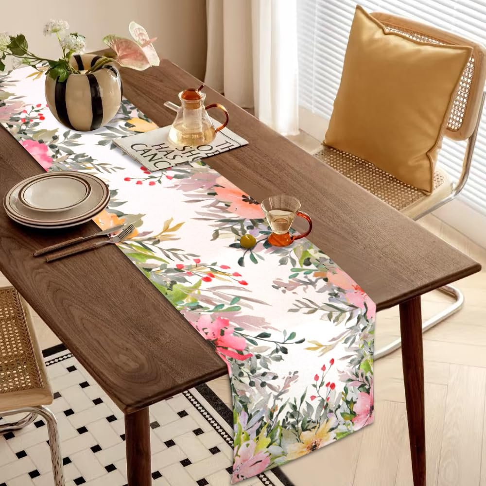 Watercolor floral table runner on a wooden dining table with place settings and a vase.