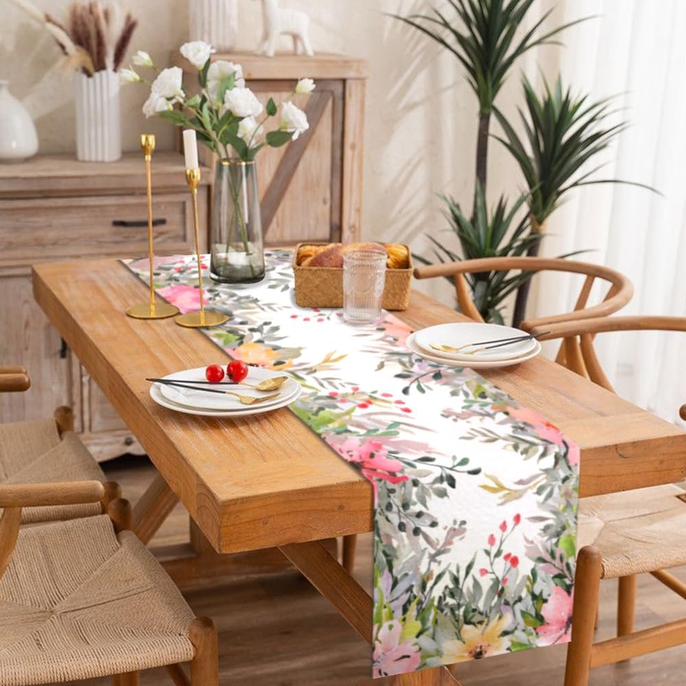 Watercolor floral table runner on a wooden dining table set for a meal, with plates, cutlery, and a glass of water.