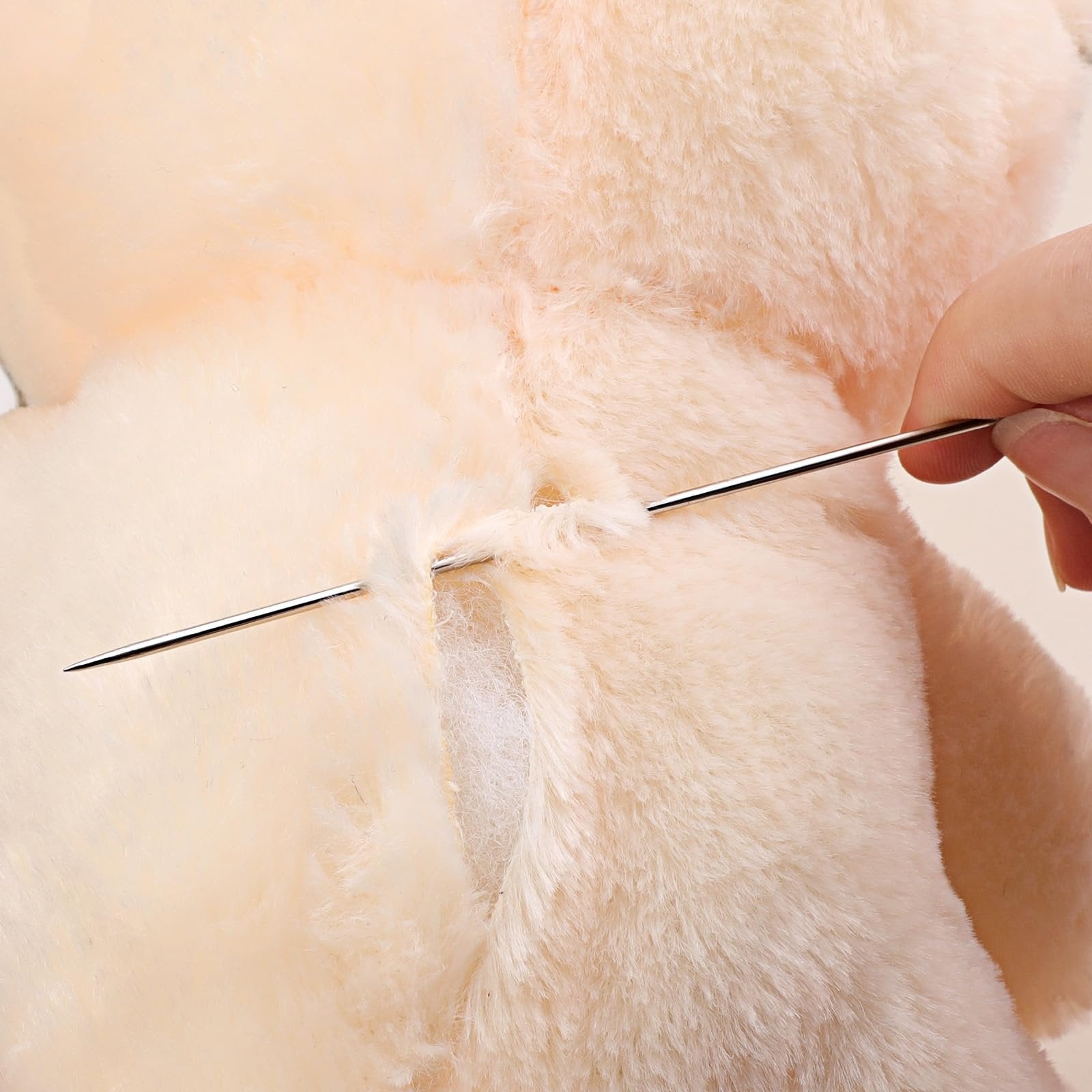 Close-up of a hand using a long sewing needle to mend a plush toy.