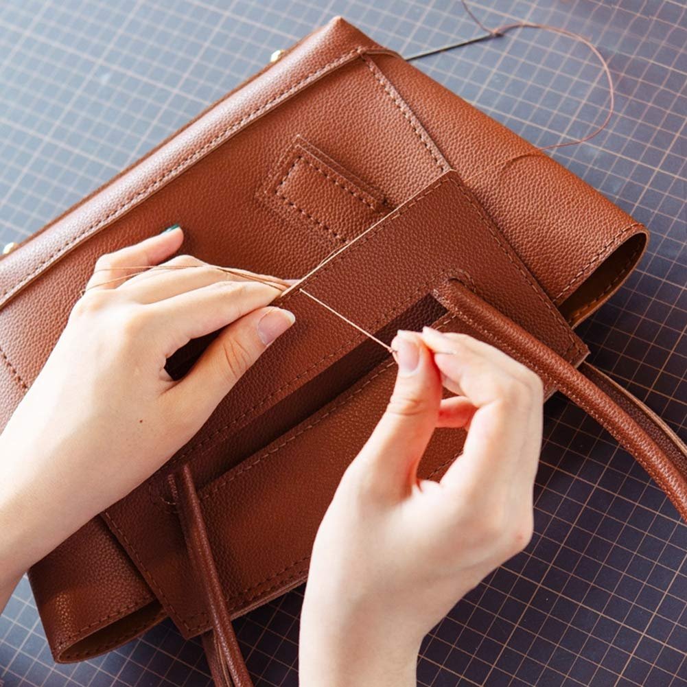 Hands sewing a brown leather bag with a needle and thread on a cutting mat