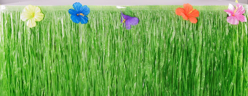 Green luau grass table skirt with colorful hibiscus flowers attached to the top edge.