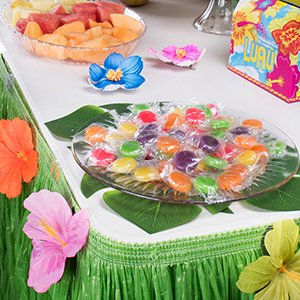 Tropical party table setting with a grass table skirt, fruit platter, and candy dish.