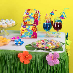 Luau party table setting with grass skirt, hibiscus flowers, cupcakes, candy, and tropical drinks.