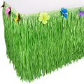 Green luau grass table skirt with colorful hibiscus flowers attached to the top edge, draped over a table.