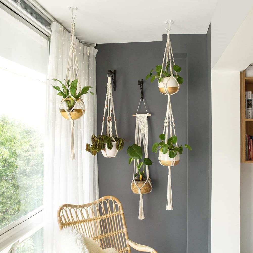Four macrame plant hangers with plants displayed in a room setting with a chair and window.