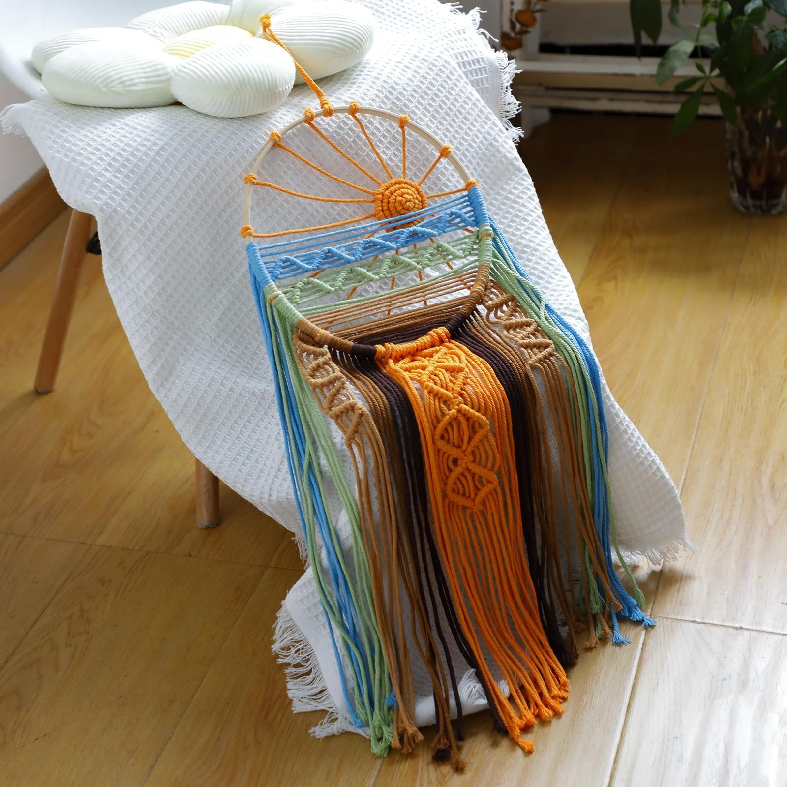 Macrame sun dream catcher with colorful woven threads and a natural wood hoop, displayed on a white textured cloth.