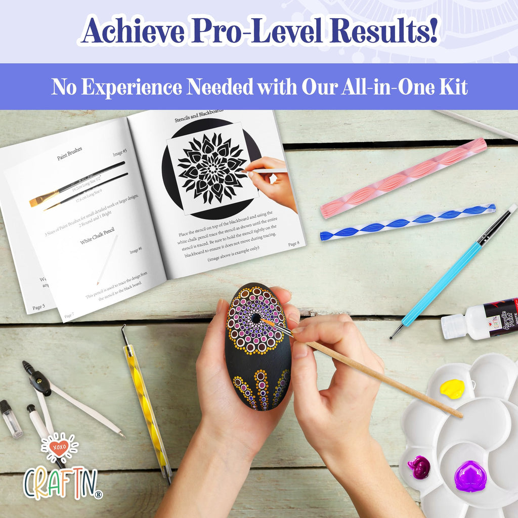 Hands painting a mandala design on a black stone with dotting tools and brushes, surrounded by kit contents.