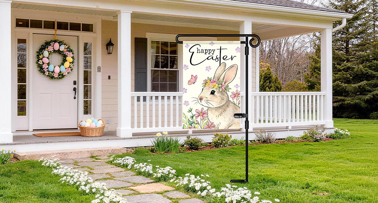 Black metal garden flag stand with a decorative Easter flag featuring a bunny and flowers, displayed on a porch.