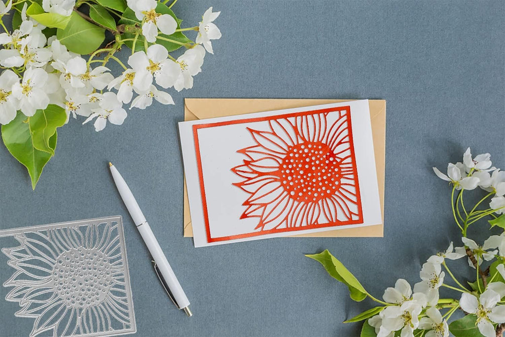 Metal sunflower cutting die and a card with a sunflower cutout, next to a pen and flowers