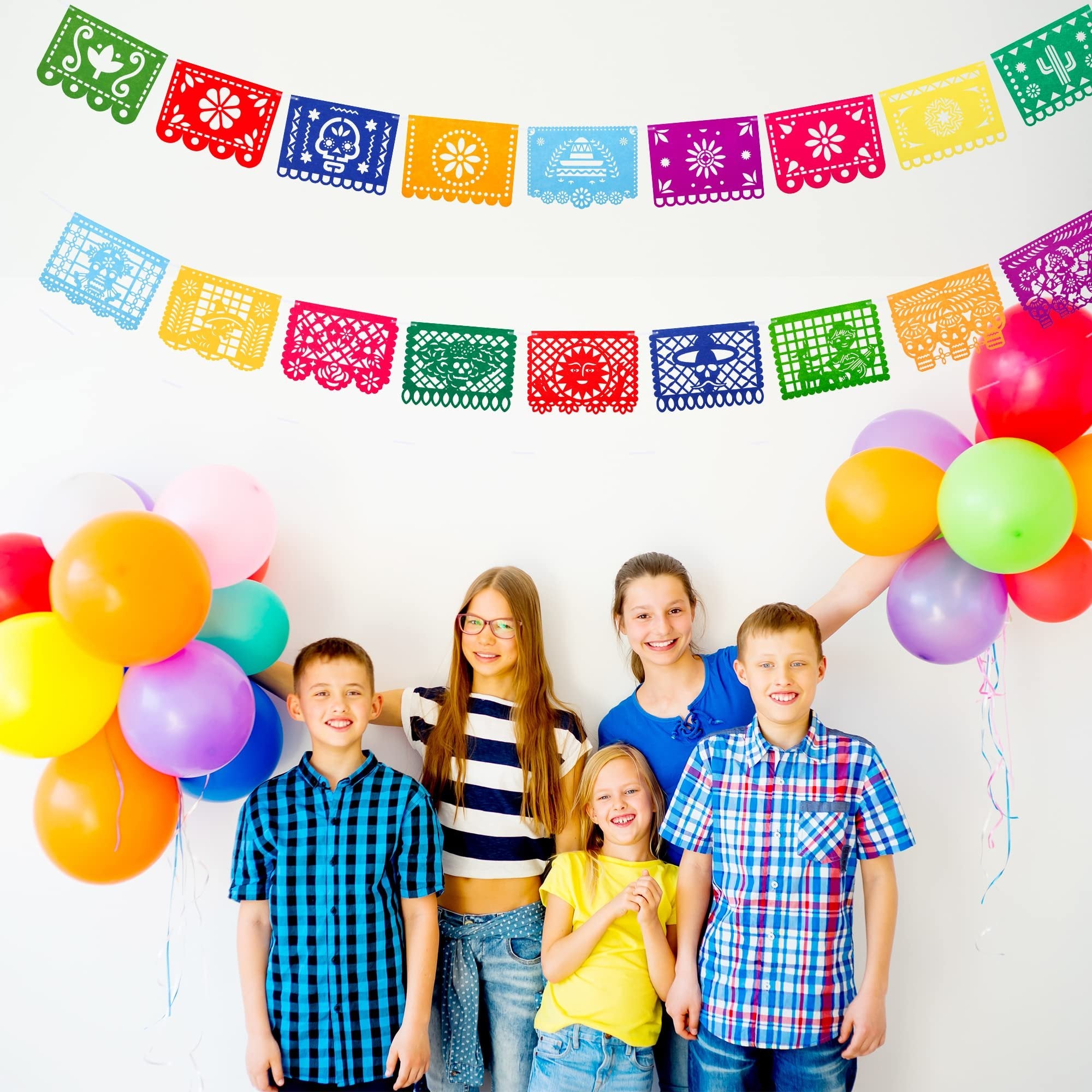Children posing with colorful Mexican fiesta papel picado banners and balloons