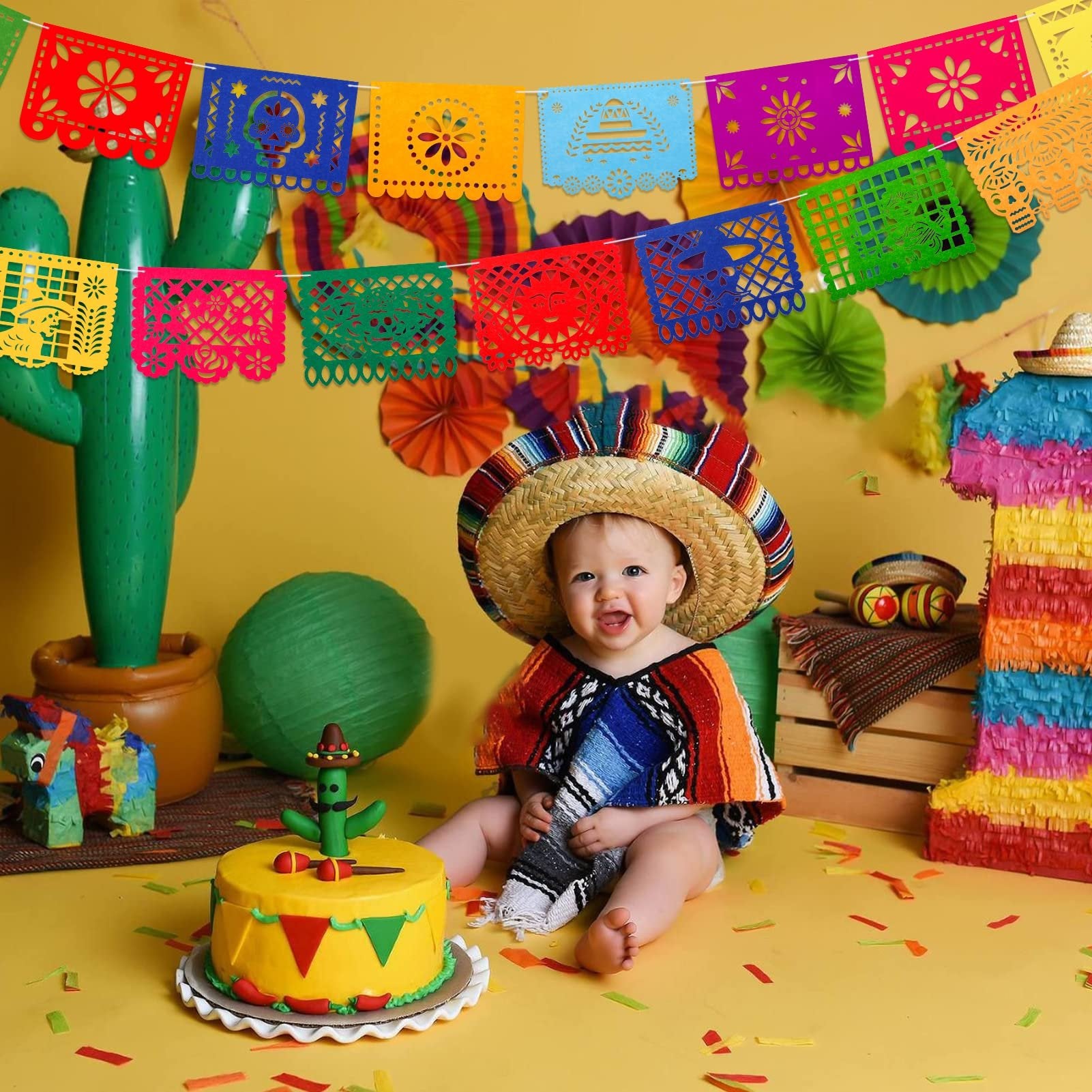 Baby in sombrero and poncho sits by a cake with cactus topper, surrounded by Mexican fiesta decorations.
