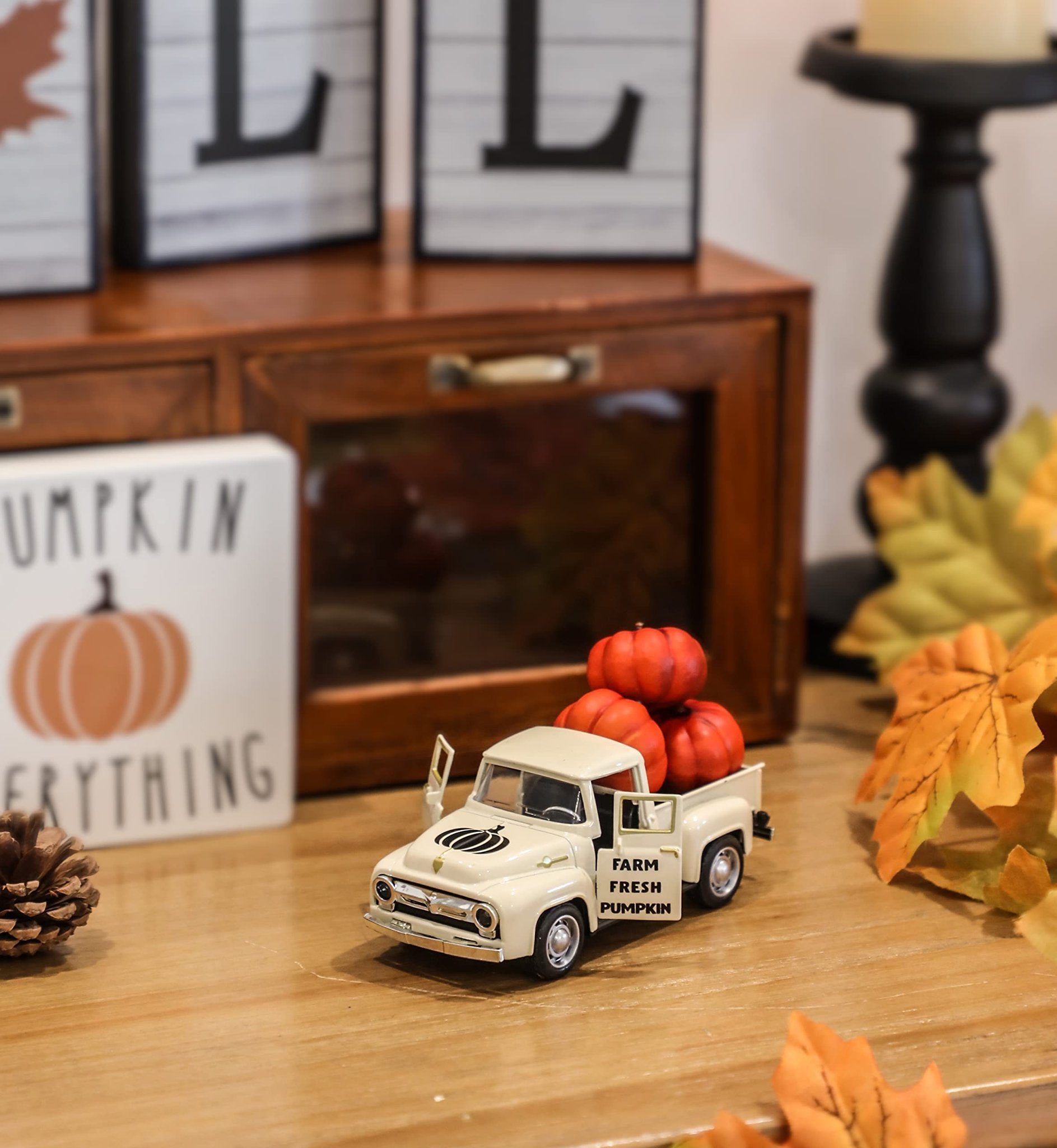 Cream metal farm truck with pumpkins in the bed, on a wooden surface with fall decor.