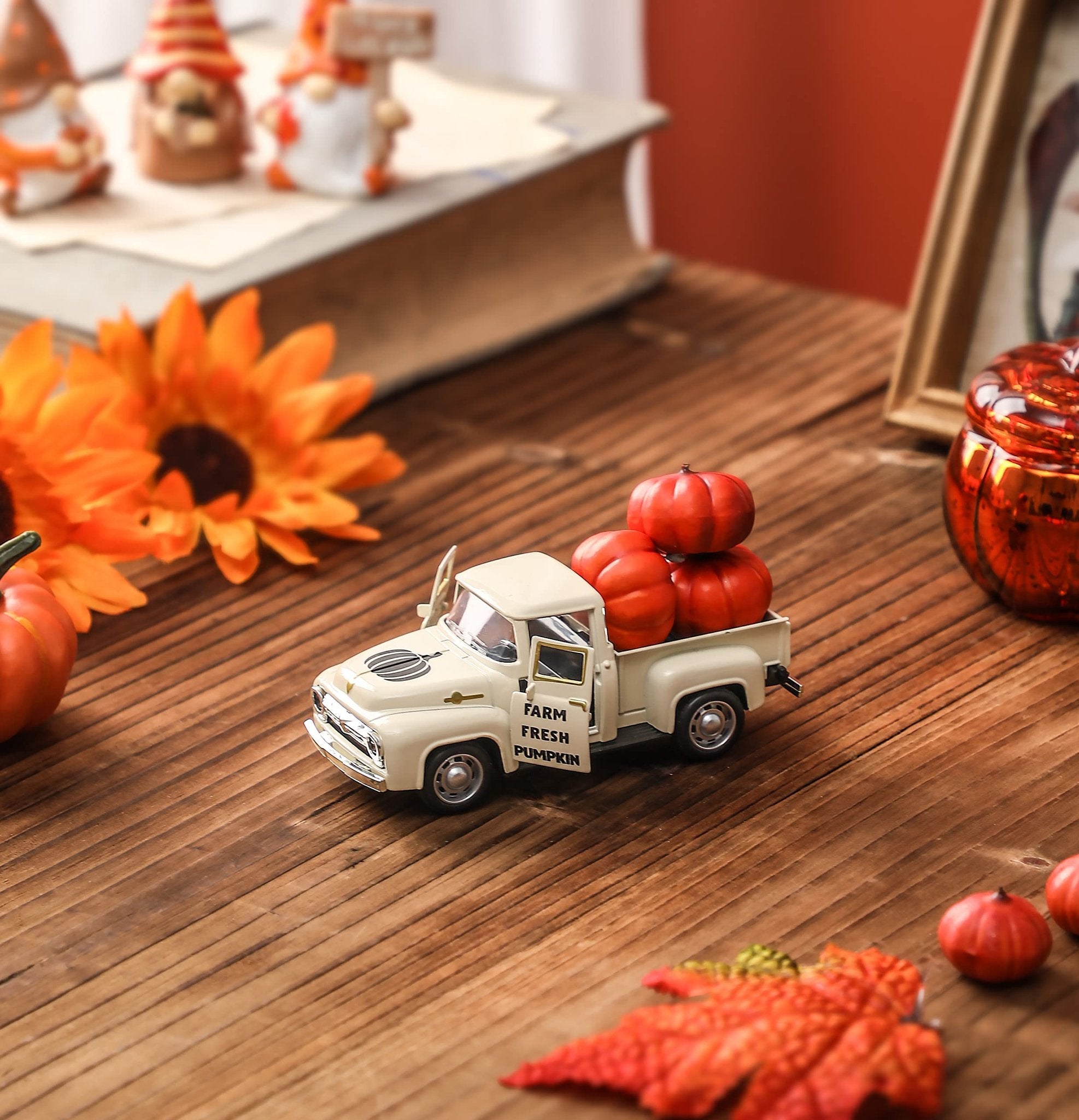 Cream colored metal farm truck with pumpkins in the bed, set on a wooden surface with fall decor.