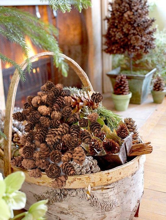 Basket filled with natural pine cones and cinnamon sticks, next to a fireplace.